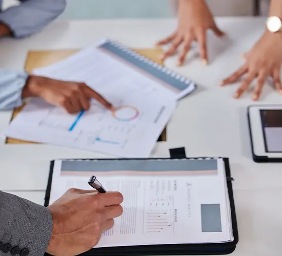 Stakeholder research and feasibility studies meeting with hands reviewing charts, reports, and a tablet—evaluating resources, risks, and timelines as part of Strategic Research & Organizational Assessment Consulting