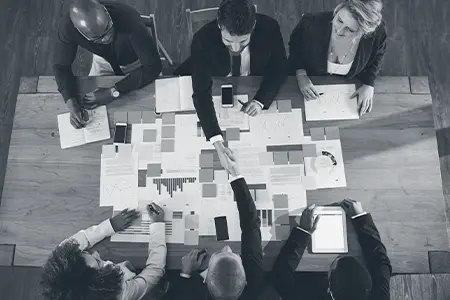 Diverse leadership team around a table reviewing data and shaking hands on a practical organizational strategy.