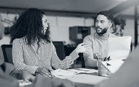 Two consultants in discussion at a meeting table, modeling transparency and honest communication during organizational consulting work.