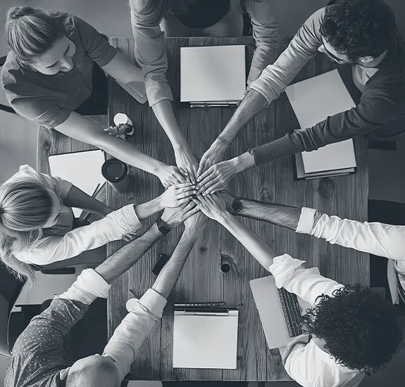 Diverse team members stacking hands at a meeting table to show unity and collaboration